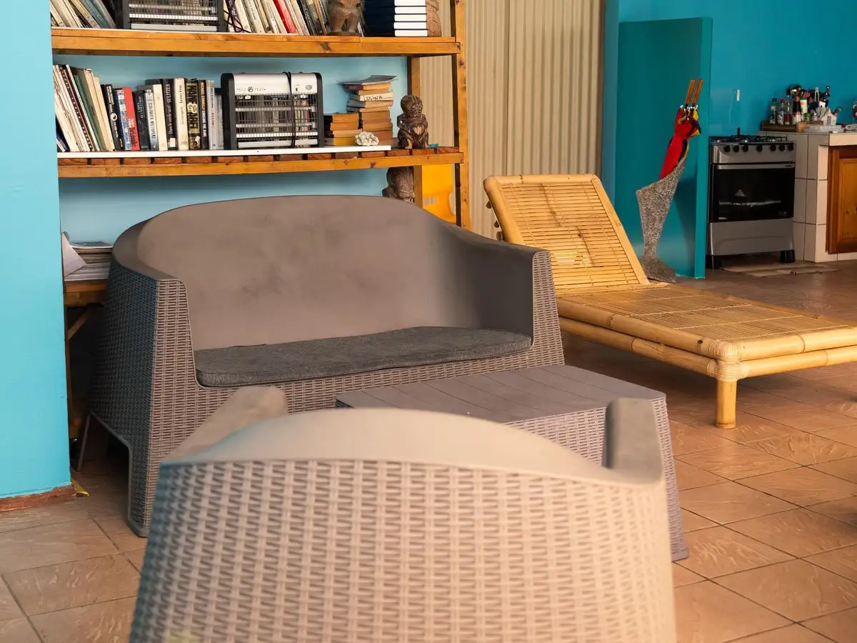 Coin bibliothèque de la Pension Ariitere avec étagères en bois, fauteuils en rotin et mur bleu