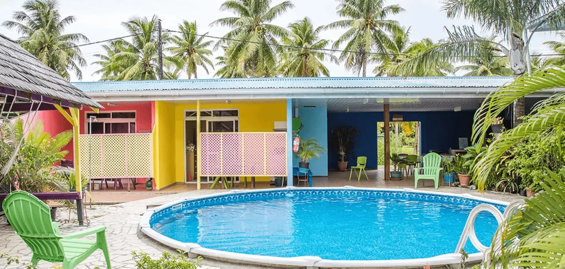 The Pension Ariitere pool in front of the colourful facades and coconut palms