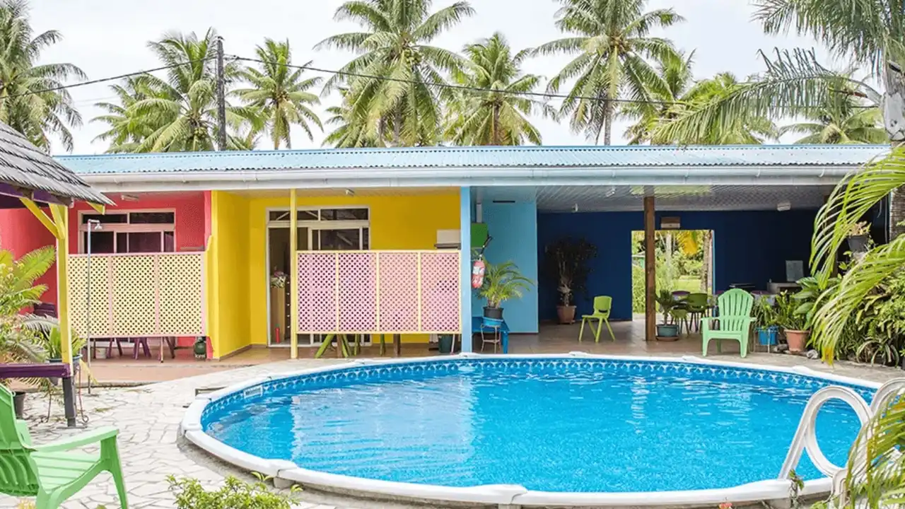 Piscine de la Pension Ariitere entourée de bungalows colorés et de cocotiers à Huahine